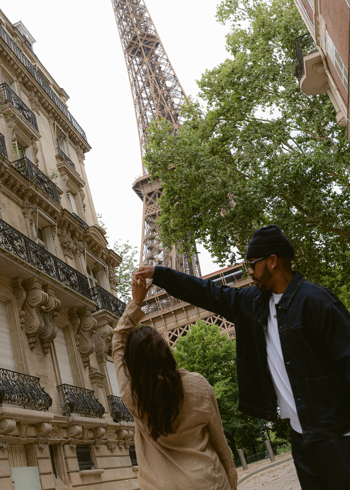 A man twirling his partner in front of the Eiffel Tower in Paris.