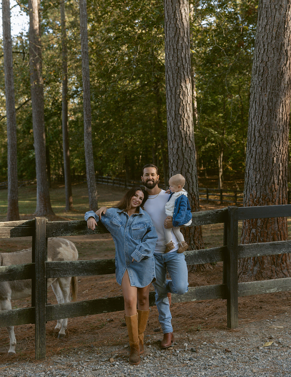 A family poses with their baby against fencing around a horse enclosure in the fall.