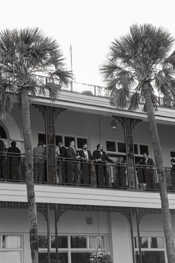 Black and white photo of wedding guests on a balcony beneath palm trees, St. Augustine, Florida