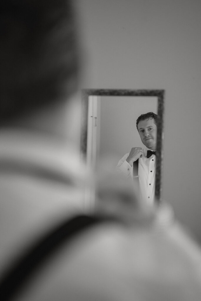 Groom adjusting his bow tie in the mirror while getting ready for his St. Augustine wedding