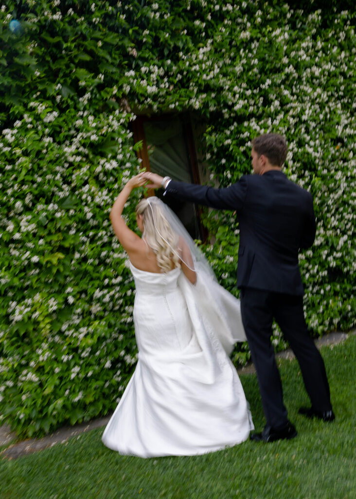 Groom playfully lifting the bride's veil by an ivy-covered wall