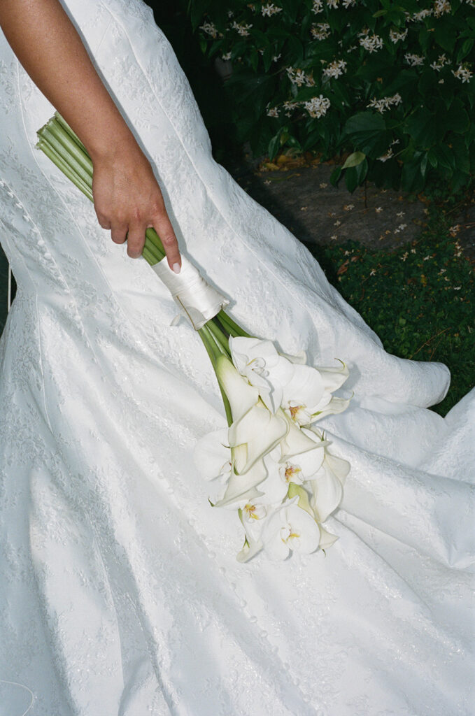 Bride holding a calla lily bouquet against her gown, garden setting