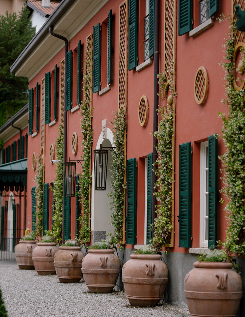 Terracotta exterior of Villa Passalacqua with potted plants and green shutters