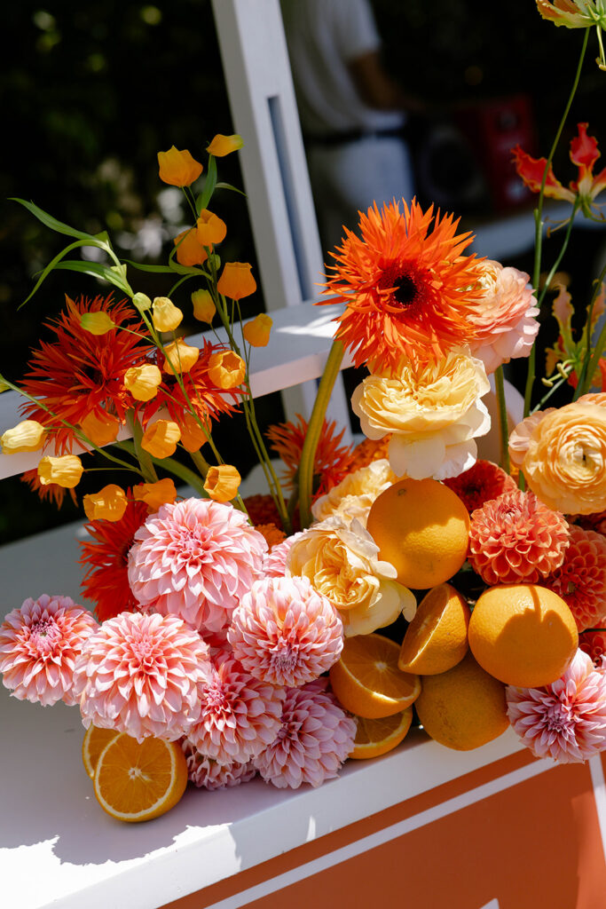 Orange dahlia and citrus floral arrangement on a wedding welcome bar cart