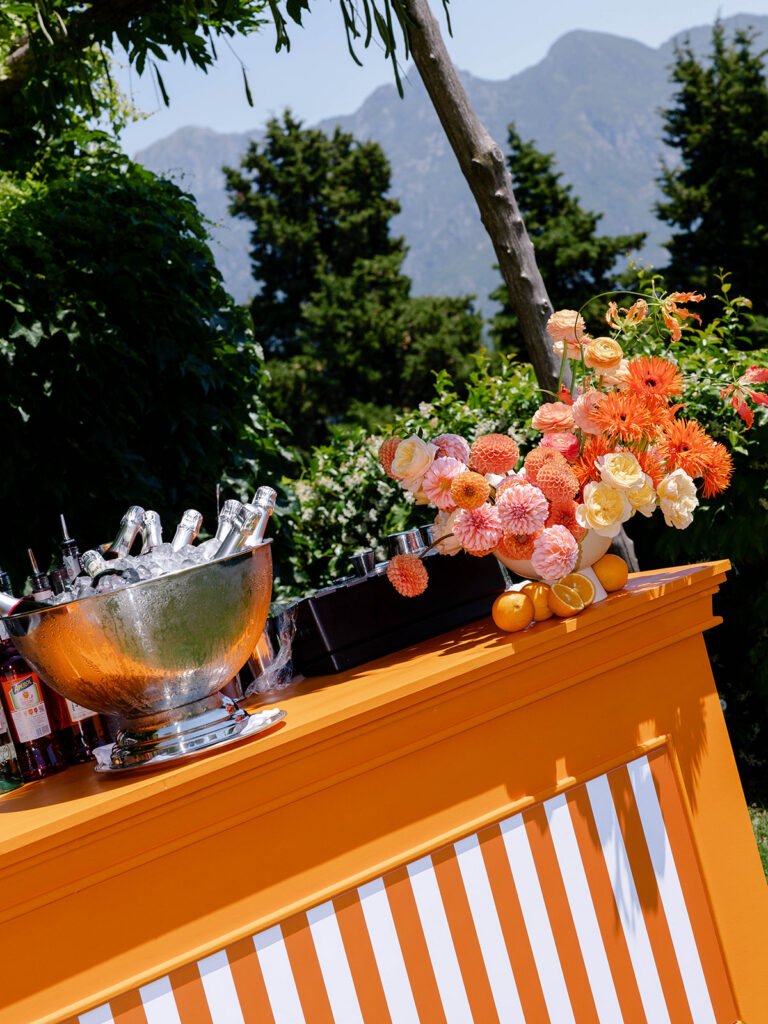 Orange floral arrangement with citrus on a wedding welcome drink cart