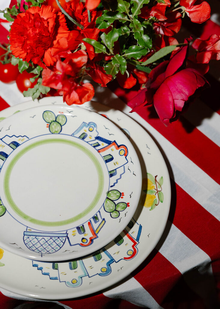 Red floral centerpiece with patterned china plate on a red and white striped tablecloth, Villa Cimbrone wedding