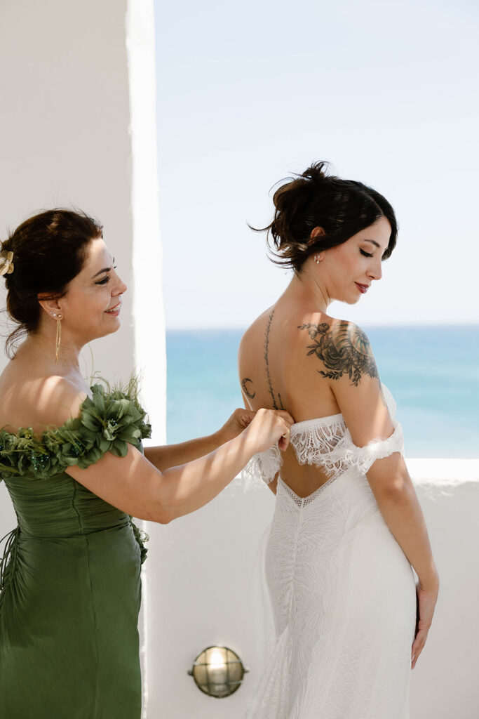 Bridesmaid helping the bride into her dress in a whitewashed courtyard