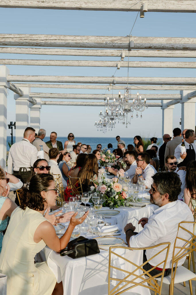 Guests seated at a reception table under a chandelier-lit pergola