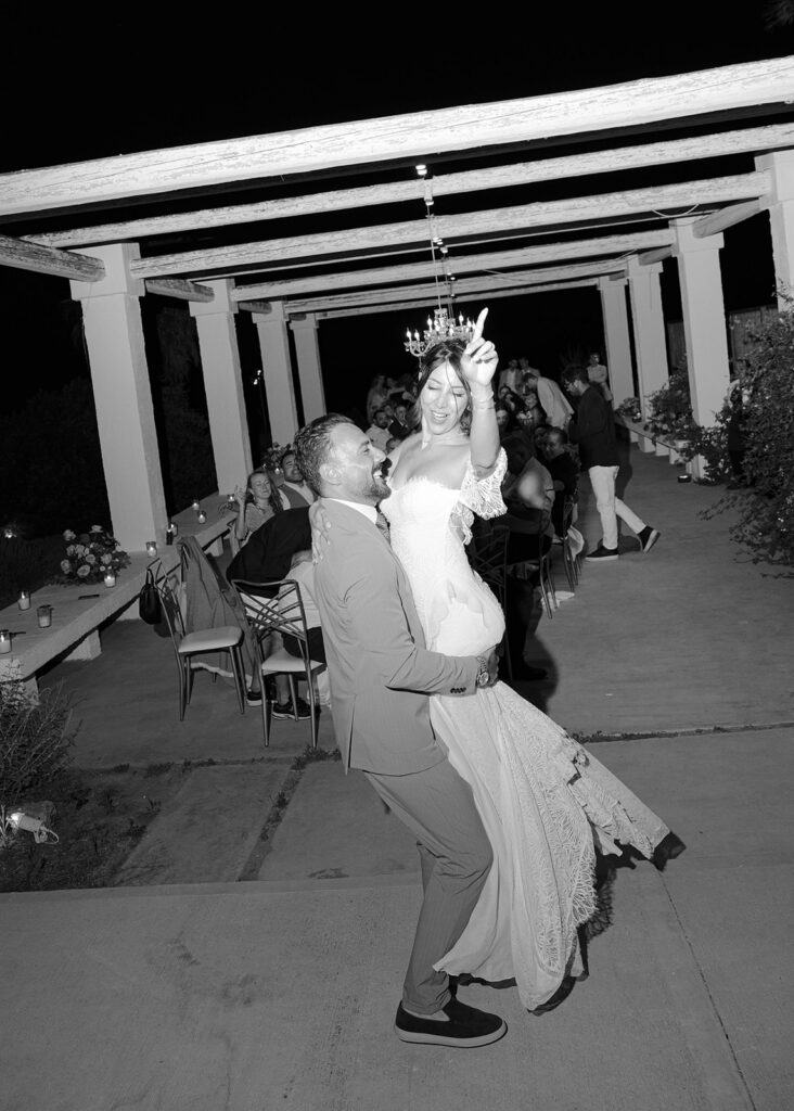 Bride and groom dancing under string lights and a chandelier pergola at night