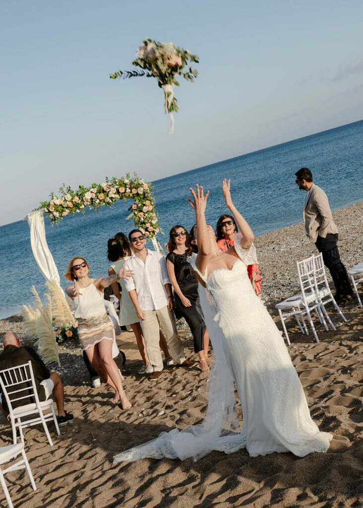 Guests cheering as the bride tosses her bouquet on the beach